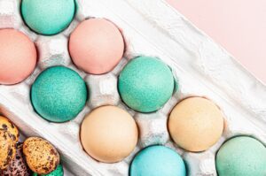 Blick in einen Eierkarton mit bunten Ostereiern und kleinen Wachteleiern in Grün, Rot und Gelb als Hinleitung zu der Frage, weshalb wir zu Ostern bemalte und gekochte Eier essen.