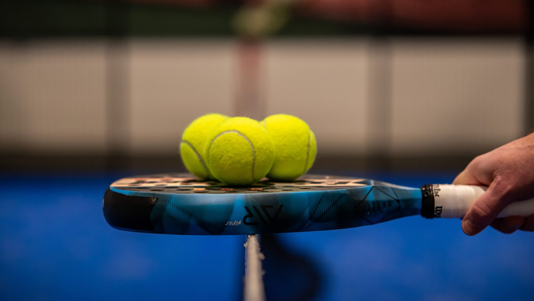 Drei Padel-Bälle und ein Padel-Racket.